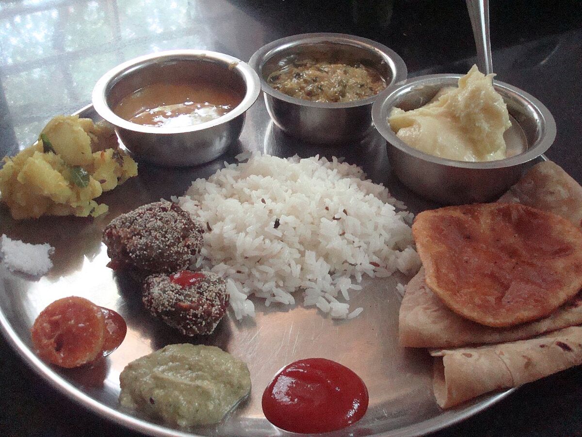 An Indian thali: rice, dal, vegetables, chutneys and flatbread on a steel plate.